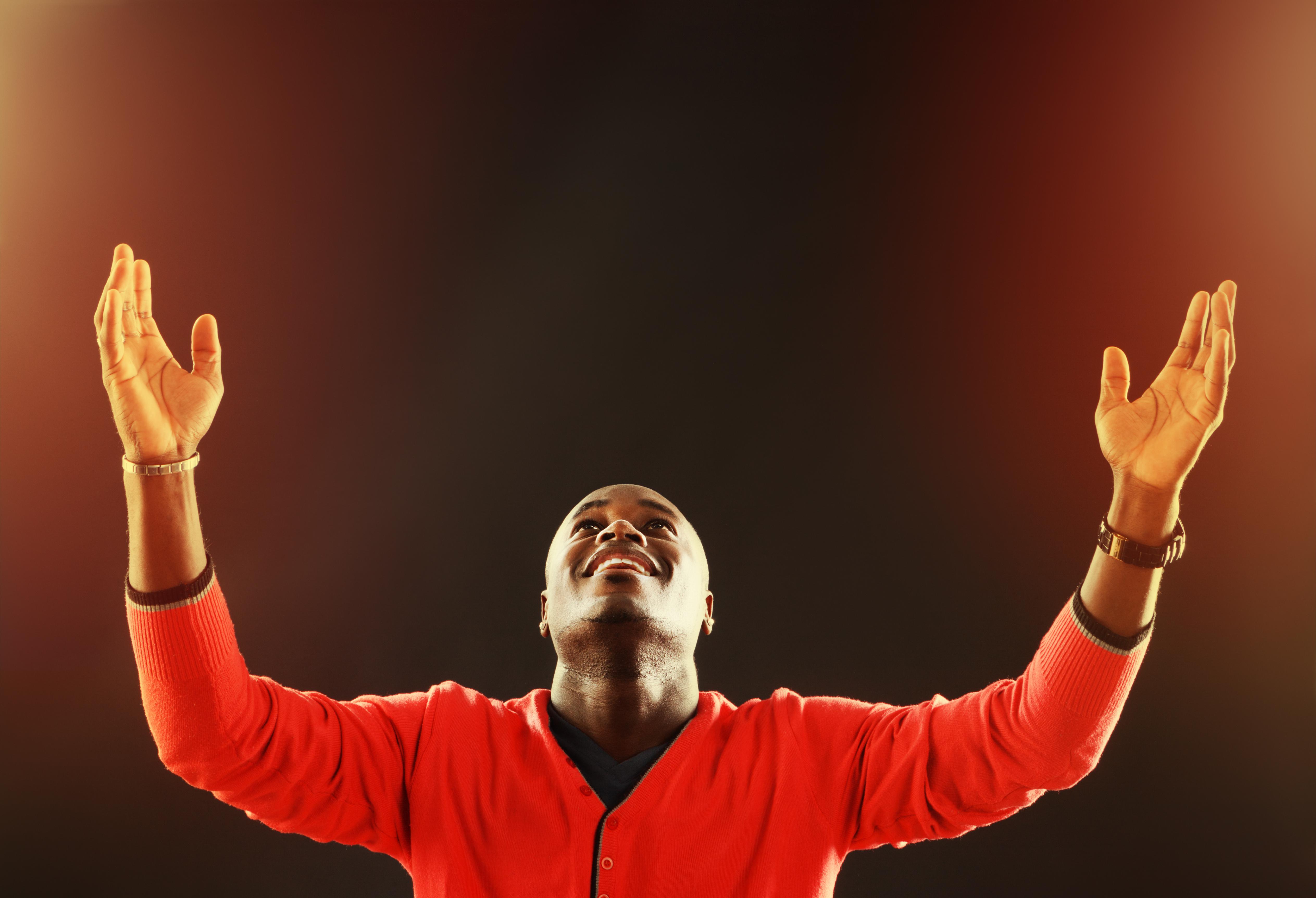 Inspired young man looks up, his hands raised in prayer
