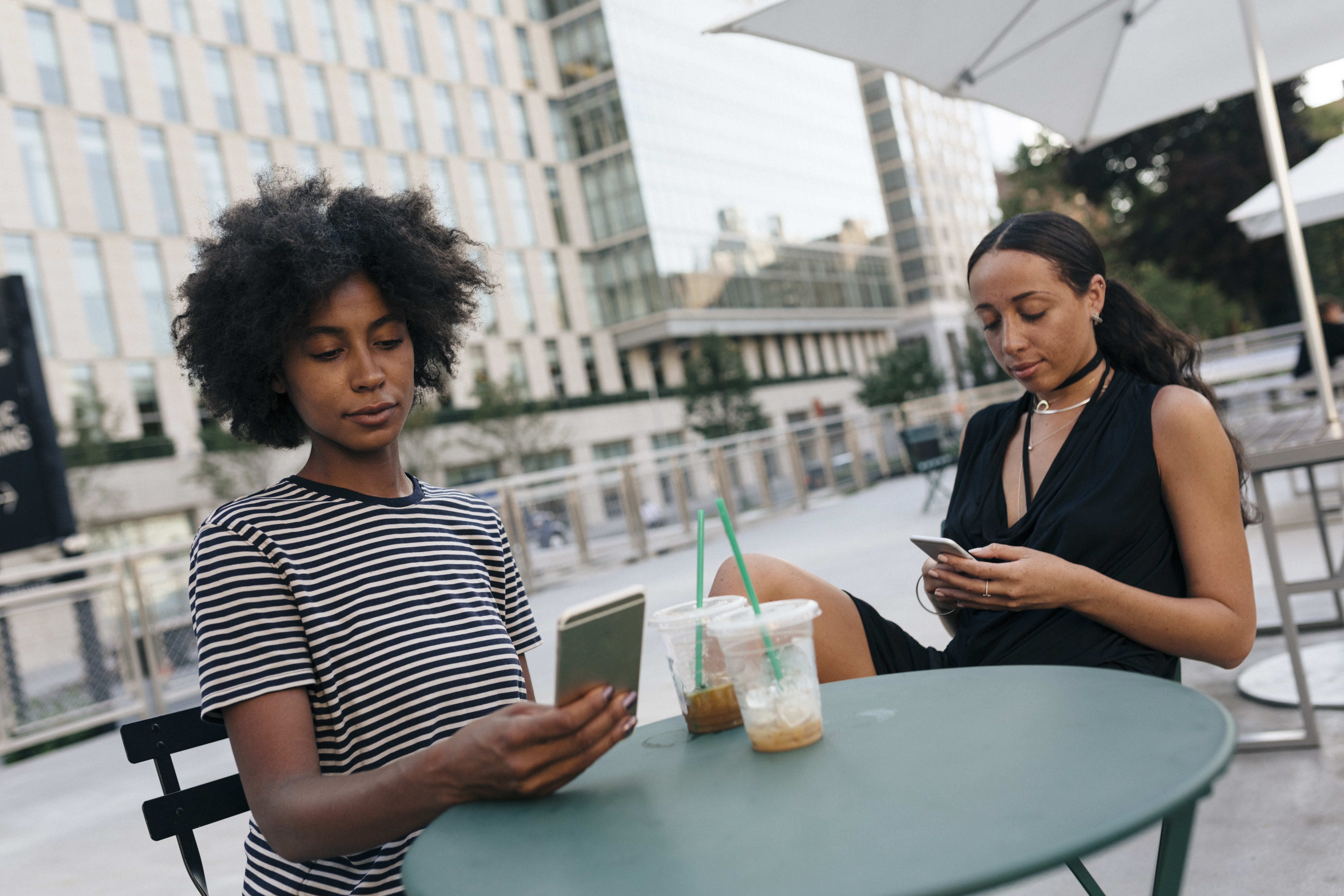 Two friends sitting at pavement cafe looking at their cell phones