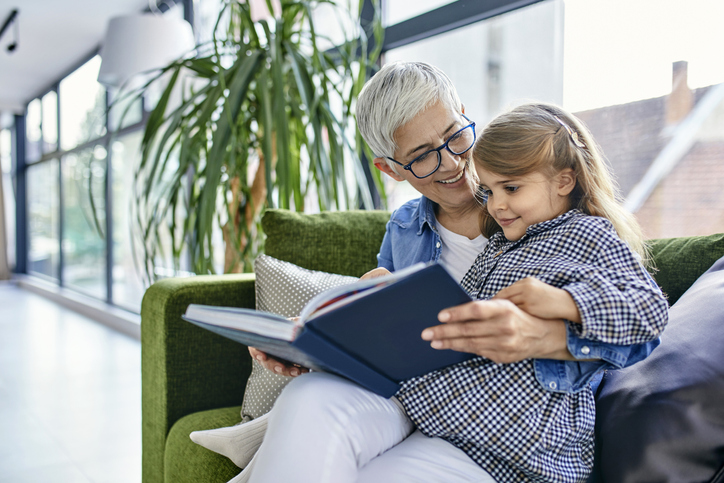 Grandmother sitting on couch with granddaughter, reading book together