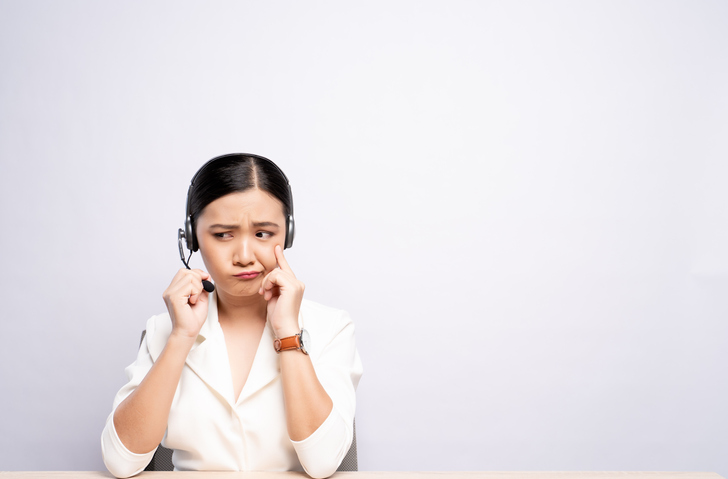 Female Customer Service Representative Talking On Headset While Sitting At Desk Against White Background