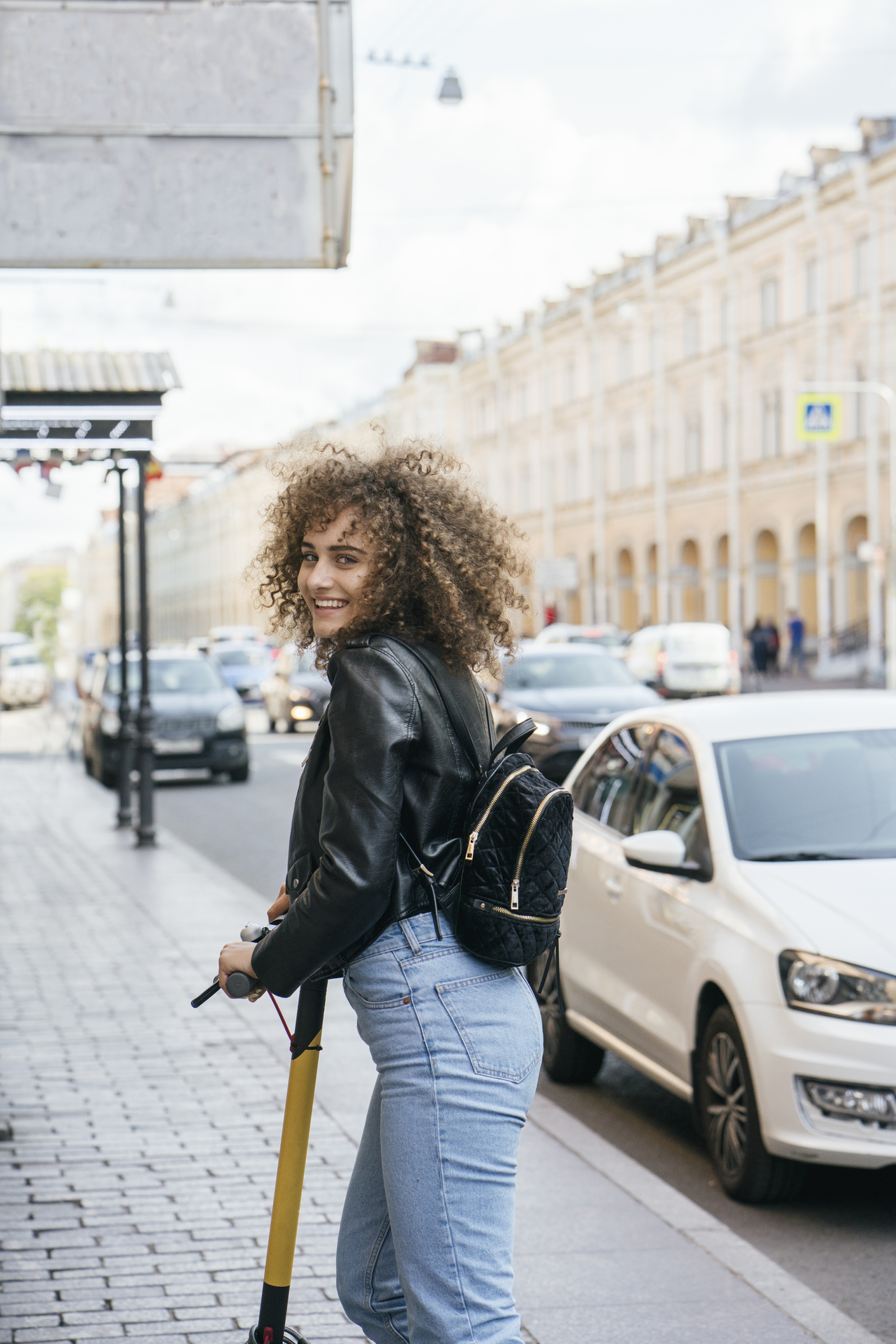 Portrait of smiling teenage girl with scooter standing on pavement