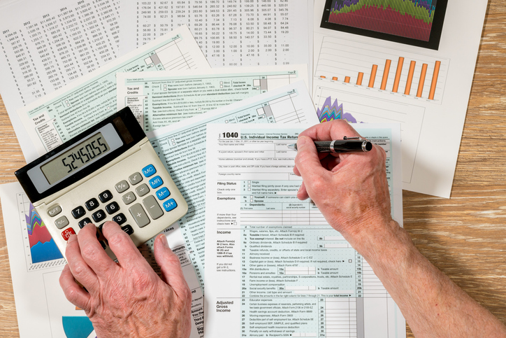 Cropped Hands Of Man Filing Documents Using Calculator At Table